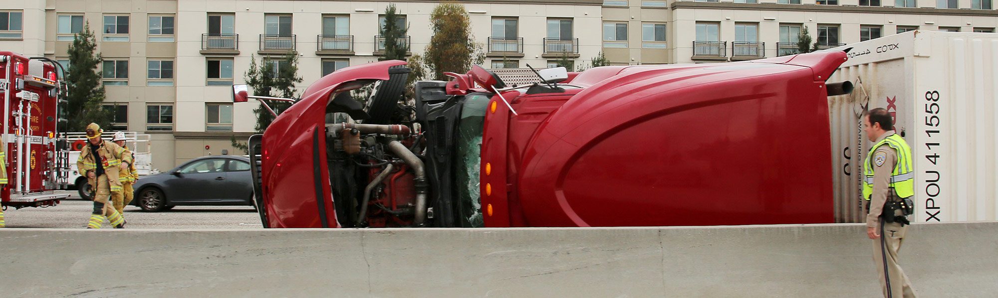 Red semi truck laying on its side after a serious accident on a busy highway.