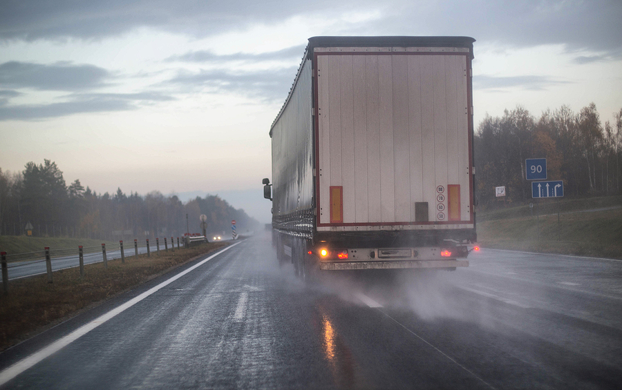 A semi-truck driving fast down a rainy highway.