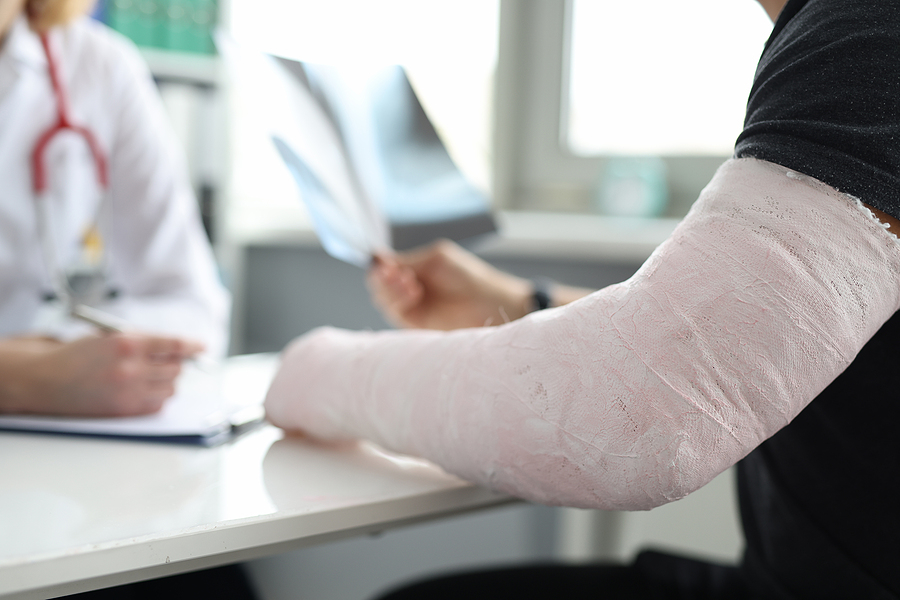 Close-up of man with broken arm at doctor appointment. Doctor at hospital prescribing treatment. Injury, accident, healthcare and medicine concept