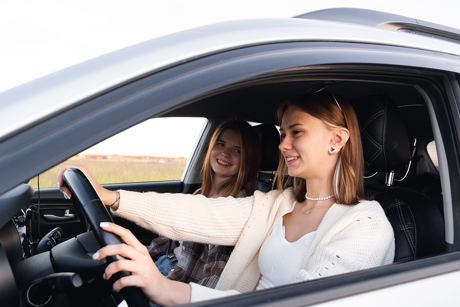 Two young women in the car together smiling while having a conversation and driving