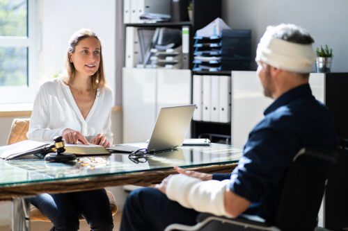 Man sitting at a lawyers desk with a cast on his arm and bandage on his head speaking to lawyer after being hurt in an accident in Waterville, Ohio. 