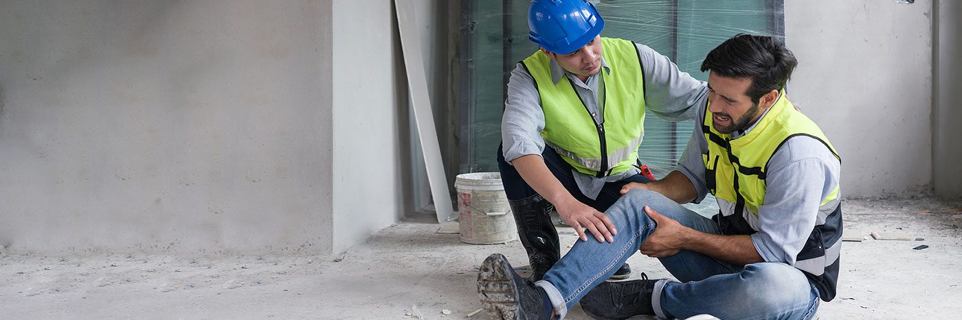 two men wearing hi-vis vests at work, one man fell and hurt his knee on the job