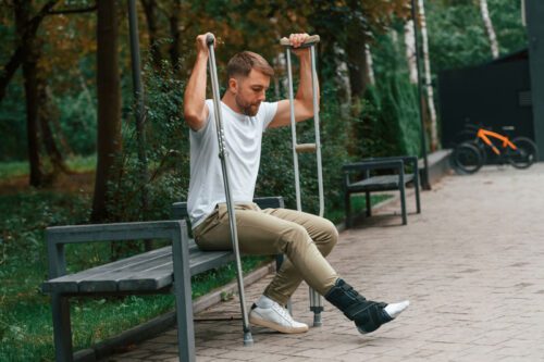 man with injured ankle sitting on park bench with crutches - if you have been injured in an accident in Whitehouse, Ohio, contact Arthur Law Firm