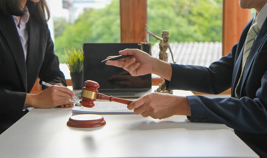 someone meeting with a lawyer, lawyer holding a gavel and describing items on paperwork to a client