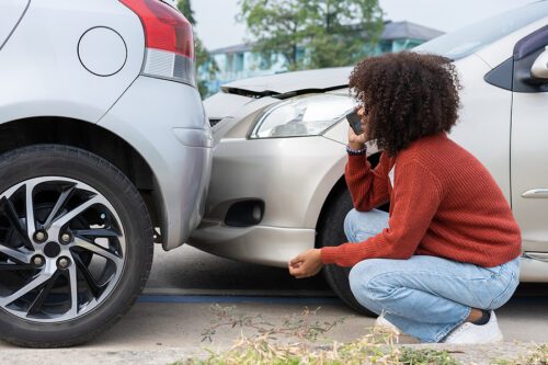 young woman talking to an oregon ohio lawyer on the phone crouching down in front of two cars after being involved in an accident
