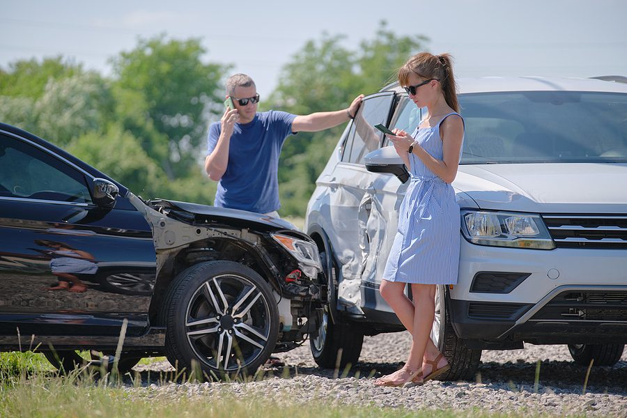 man and woman standing outside at the scene of a car accident contacting people on their phones