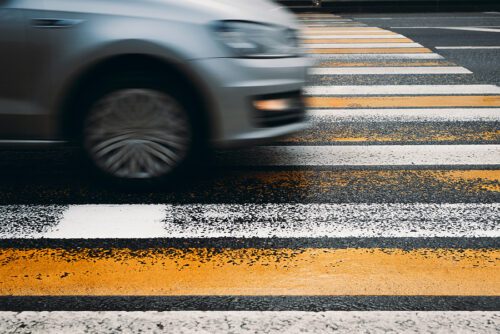 blurred car driving over pedestrian walkway on road - risk of pedestrian accident