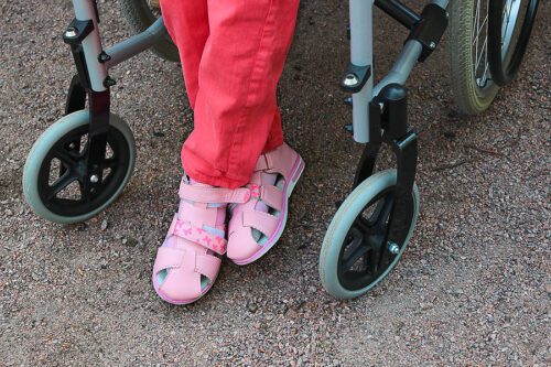 Photo of a disabled child's pair of pink shoes while sitting in a wheelchair. 