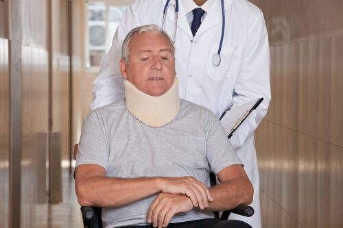 Older man sitting in a wheelchair wearing a neck brace.