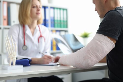 Patient with plaster cast on broken arm consults doctor in hospital. Professional treatment of injuries and broken arm after a car accident.