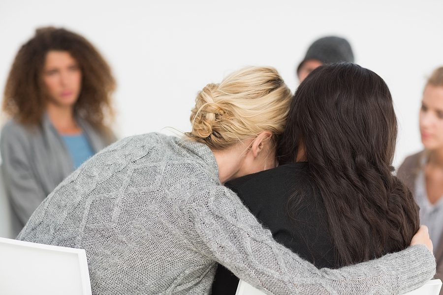 Two women embracing in rehab group at therapy session. 