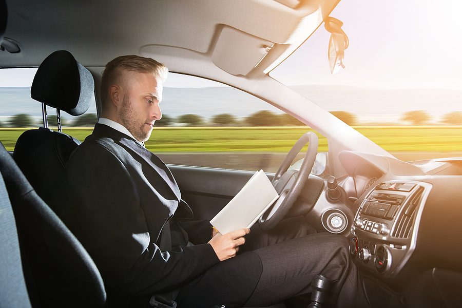 Young businessman sitting inside self driving car and reading book. 