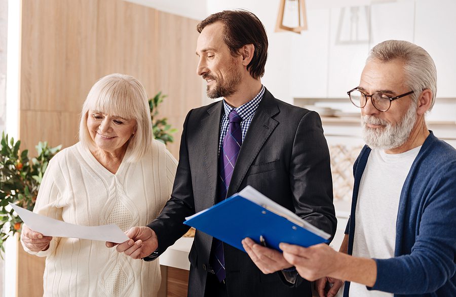 Older couple shaking male attorney's hand as he helps them with paperwork. 