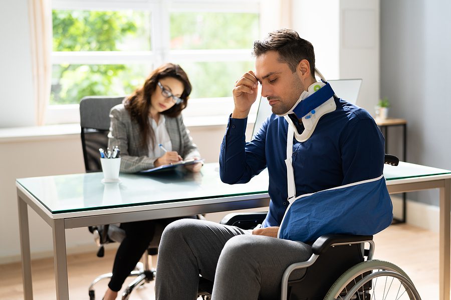 Injured man in wheelchair wearing an arm sling meeting with female attorney. 