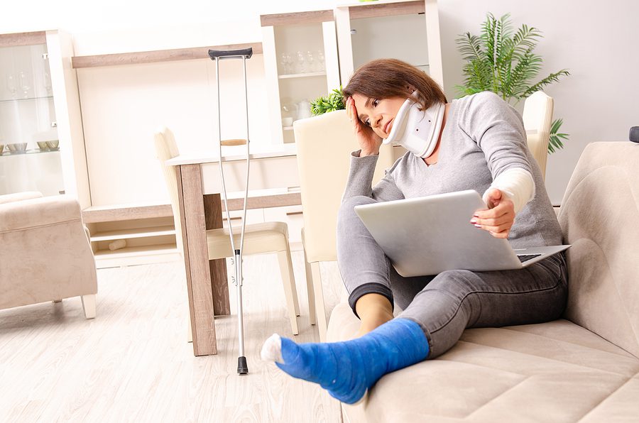 Woman sitting on her couch wearing a cast and neck brace, trying to recover from car accident injuries. 