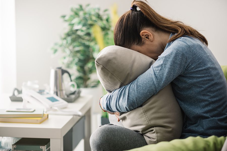 Stressed woman sitting on the couch with her face in a pillow. 