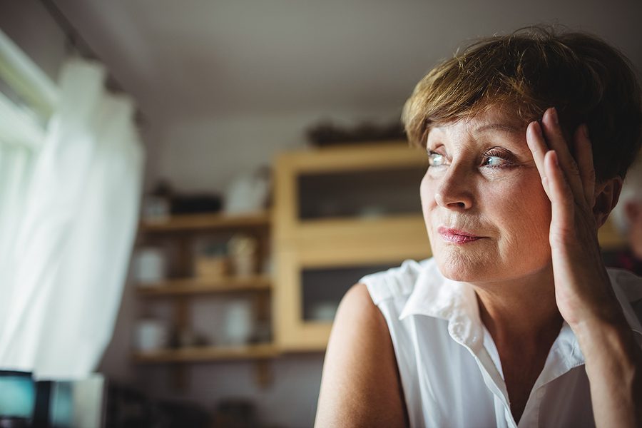 Worried senior woman looking out the window with her hand on forehead.