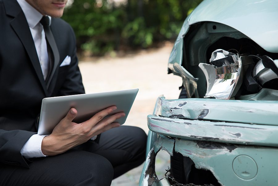 Insurance adjuster examining a car at an accident scene and taking notes. 