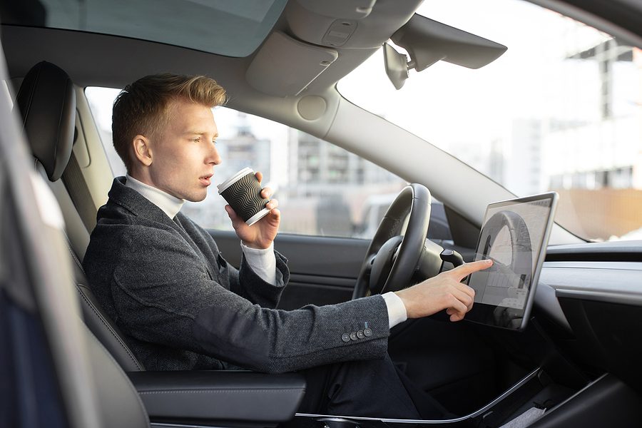 Male businessman wearing a suit and drinking coffee while touching the navigation screen of a self driving car. 