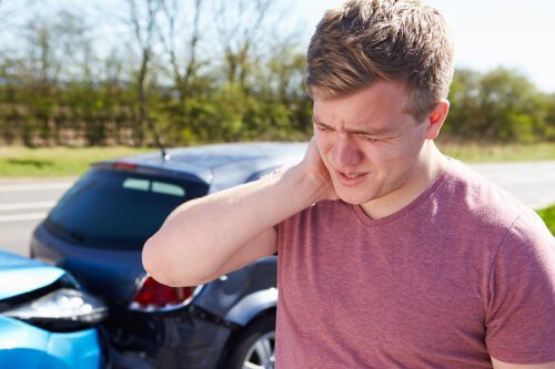 Male standing in front of a car accident scene, holding his neck. 