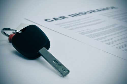 Close up of a car key lying on top of a rental car insurance policy. 