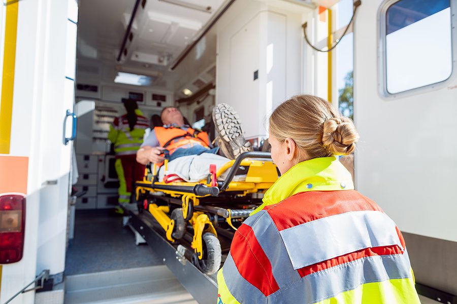 Paramedics in uniform putting an injured man on a stretcher into an ambulance. 