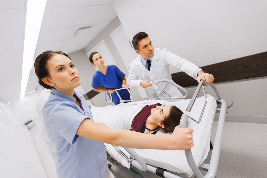 Injured woman in a hospital being pushed down the hall on a gurney by medical professionals.