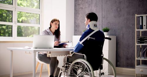 Injured male in a wheelchair sitting at a desk discussing his case with a female attorney. 