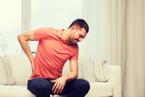 Injured man sitting on couch holding his lower back in pain. 