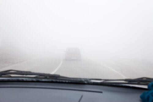 Driver's view of a car in front of them in foggy conditions. 