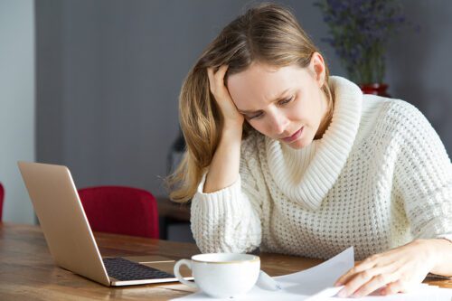 Woman holding her head in her hand, while looking at a document with confusion and frustration. 