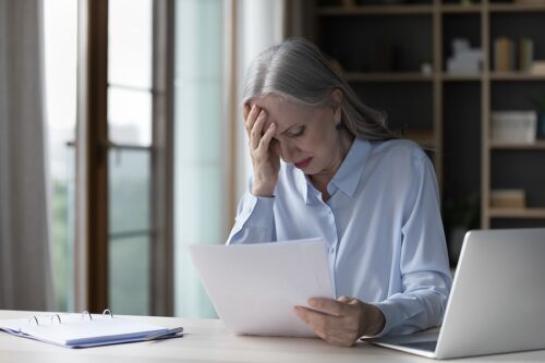 Older woman reading a letter she received and looking stressed. 