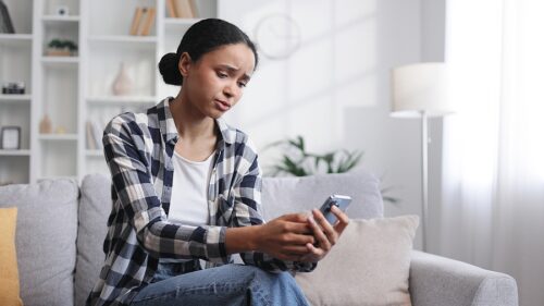 Worried woman sitting on the couch, holding her phone in her hand and waiting for a phone call. 