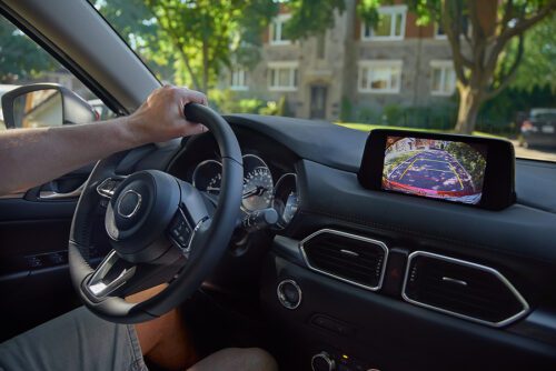 Driver with hands on steering wheel, using the car's backup camera to reverse.