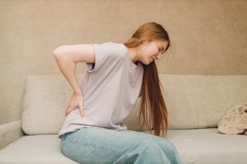 Woman sitting on her couch, holding her pack and wincing in pain.
