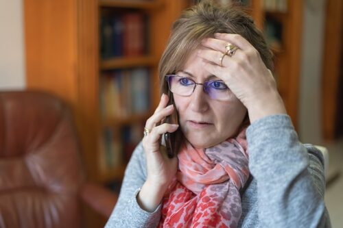 Woman talking on the phone with her hand on her forehead and looking stressed. 