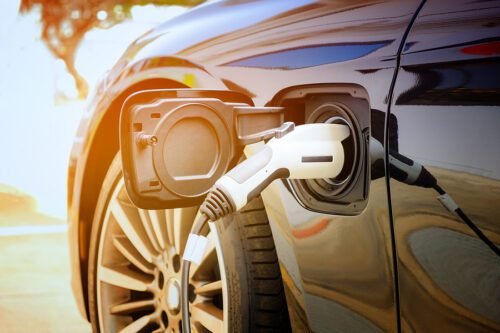Closeup of a black electric vehicle with a charger plugged into the battery