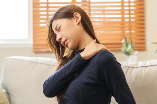 Woman sitting on couch with muscle pain in her neck and shoulders. 