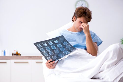 Male patient sitting on a hospital bed holding his scan results and looking stressed. 