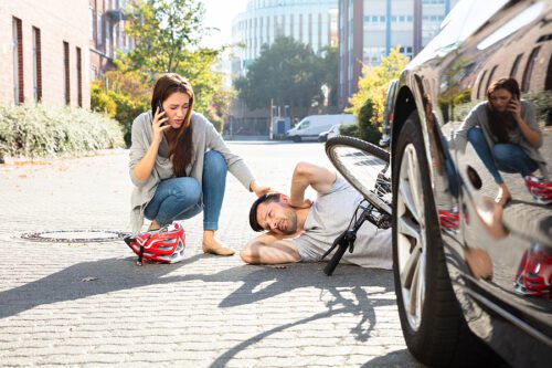 Woman kneeling down to a bicyclist she hit with her car, calling an ambulance. 