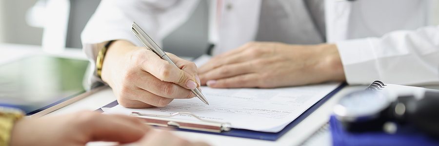 Closeup of a physician taking notes while talking to a patient.